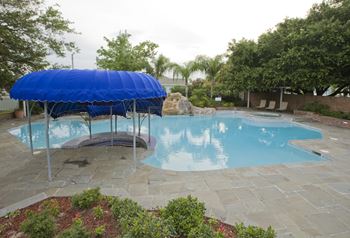 a swimming pool with a blue canopy and a rock waterfall in the background